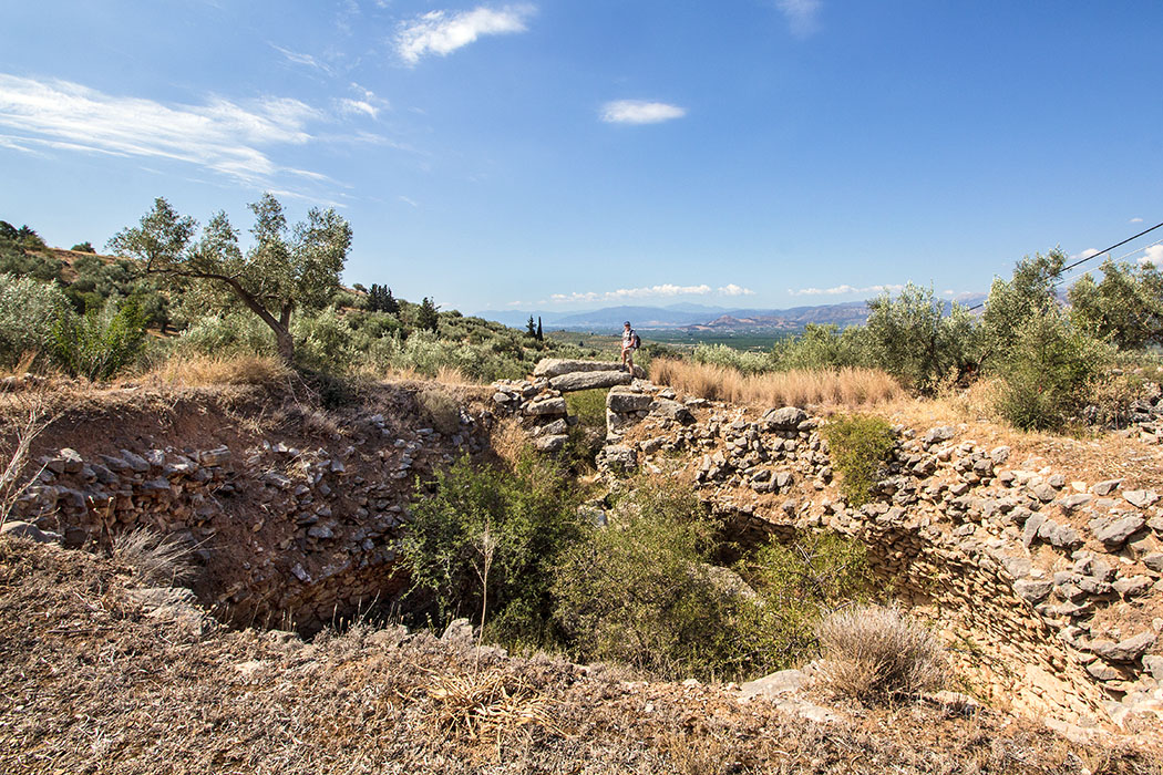 Mycenae epano phournos tholos tomb panagitsa hill argolis peloponnes greece Das Grab von Epano Phournos zählt mit dem Kyklopengrab zu den beiden ältesten Gräbern Mykenes. Hans steht auf einem der Torsteine über dem Eingang in das Grabrund mit elf Metern Durchmesser.