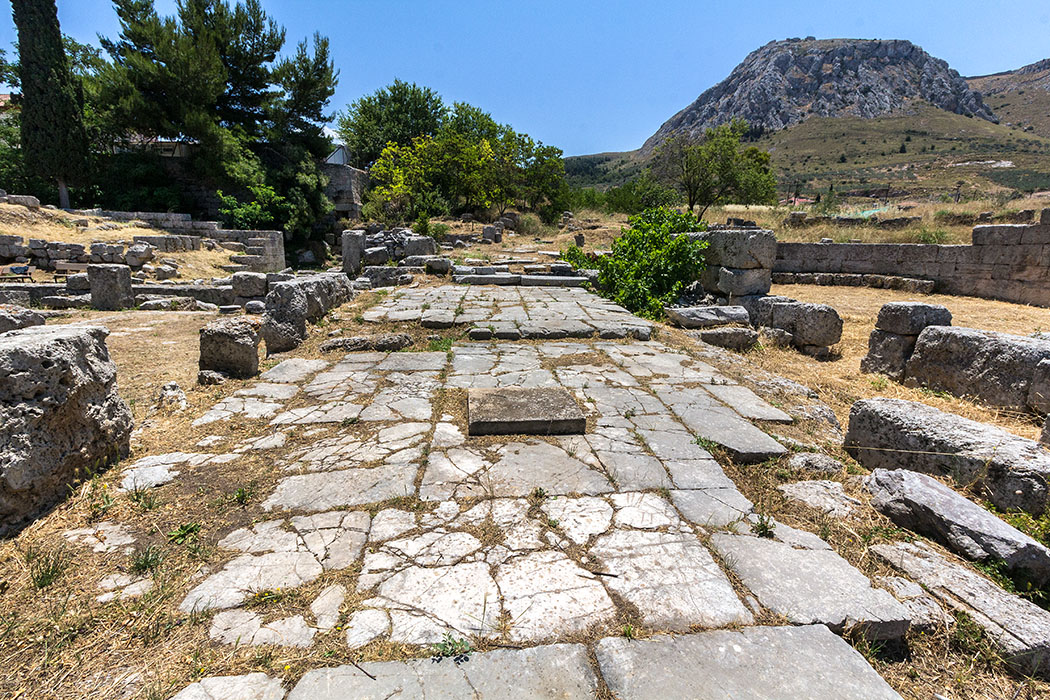 korinth bouleuterion peloponnes griechenland Im elliptisch geformten Saal des Buleuterions (Rathaus) trafen sich die Senatoren und Stadträte von Korinth. Die Ruine der Anlage befindet sich rechts, neben der gepflasterten Straße.