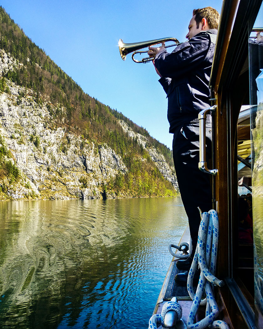 Deutschland, Oberbayern, Nationalpark Berchtesgaden, Koenigssee, Echowand, Schoenau, Bootsfahrt, April 2017 - Atemlose Stille im Boot: Unser Bootsbegleiter führt uns mit wunderbarem Trompetenspiel das Echo an der "Echowand" vor.