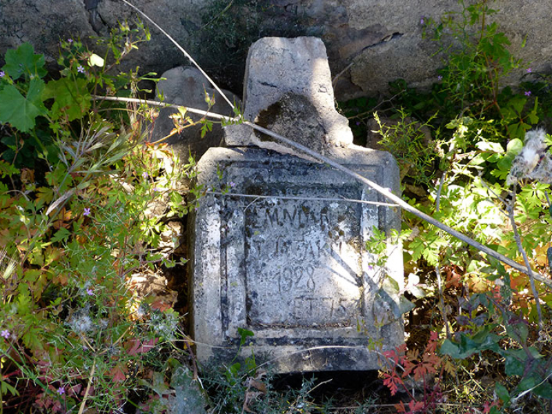 Ein alter Grabstein lehnt an der Friedhofsmauer.