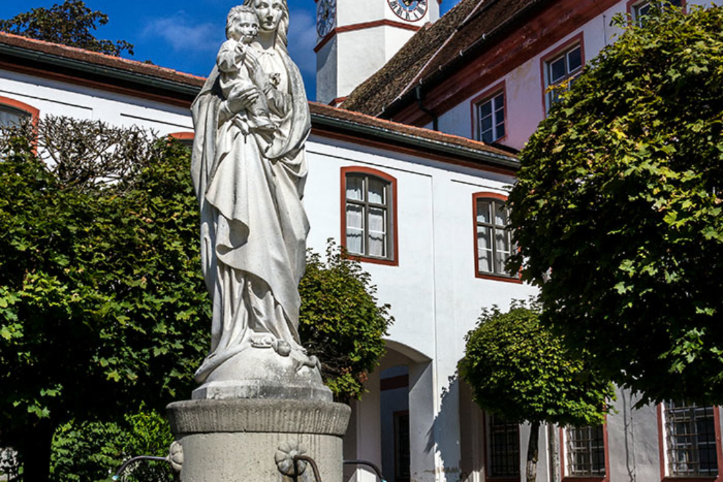 Der Marienbrunnen im Vorhof mit dem Turm der Stiftskirche Peter und Paul.